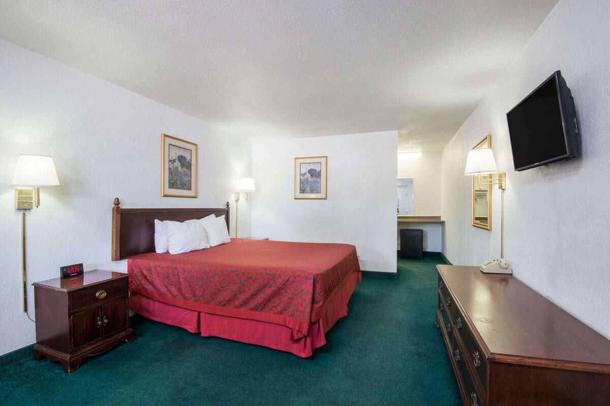 Una habitación de hotel con cama, lámparas de noche, televisor y cómoda.