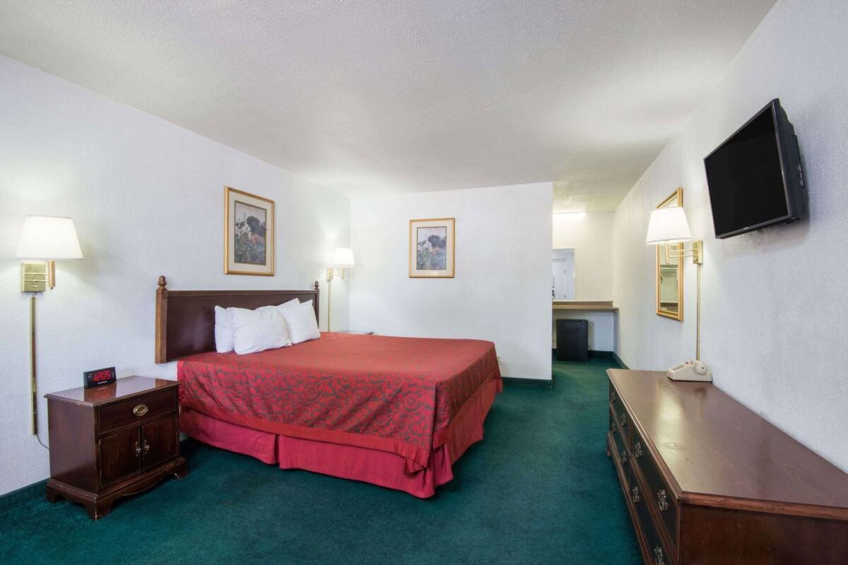 Habitación de hotel con cama, lámparas de noche, televisión, cómoda y un pequeño escritorio con lámpara.
