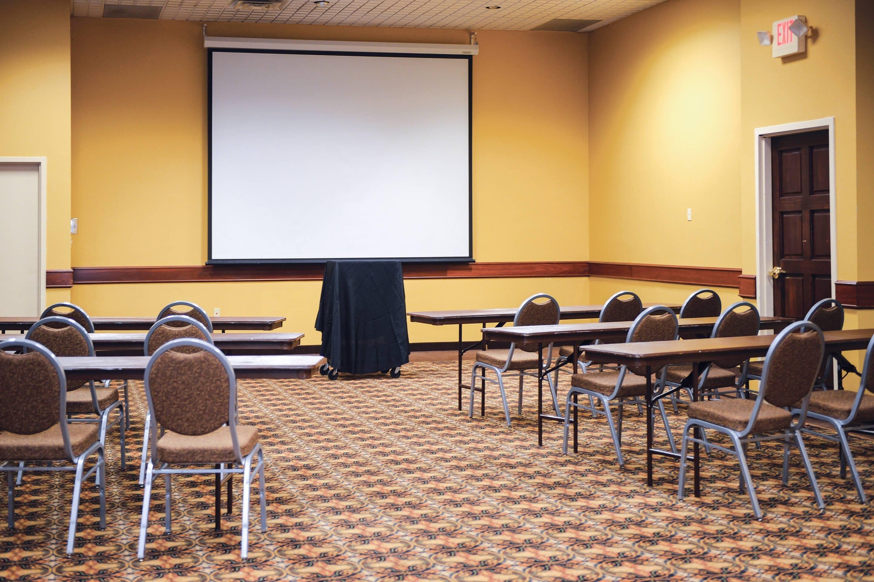 A conference room with a carpeted floor, a projector screen, and rows of chairs.