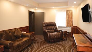 Una sala de estar con un sofá de cuero marrón, un sillón reclinable de cuero, una mesa de centro de madera y un televisor de pantalla plana montado en la pared.