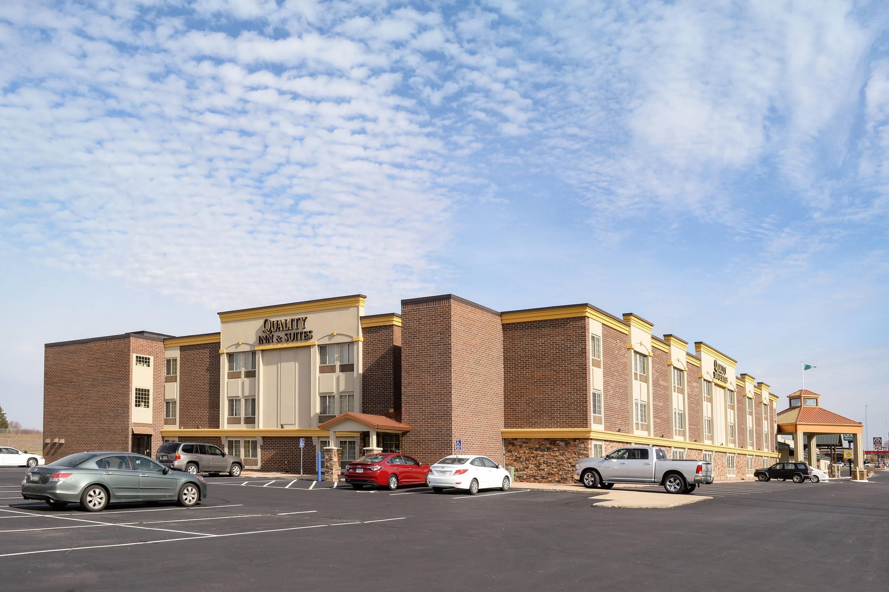 A hotel with a brick facade, multiple parking spaces, and a clear sky.
