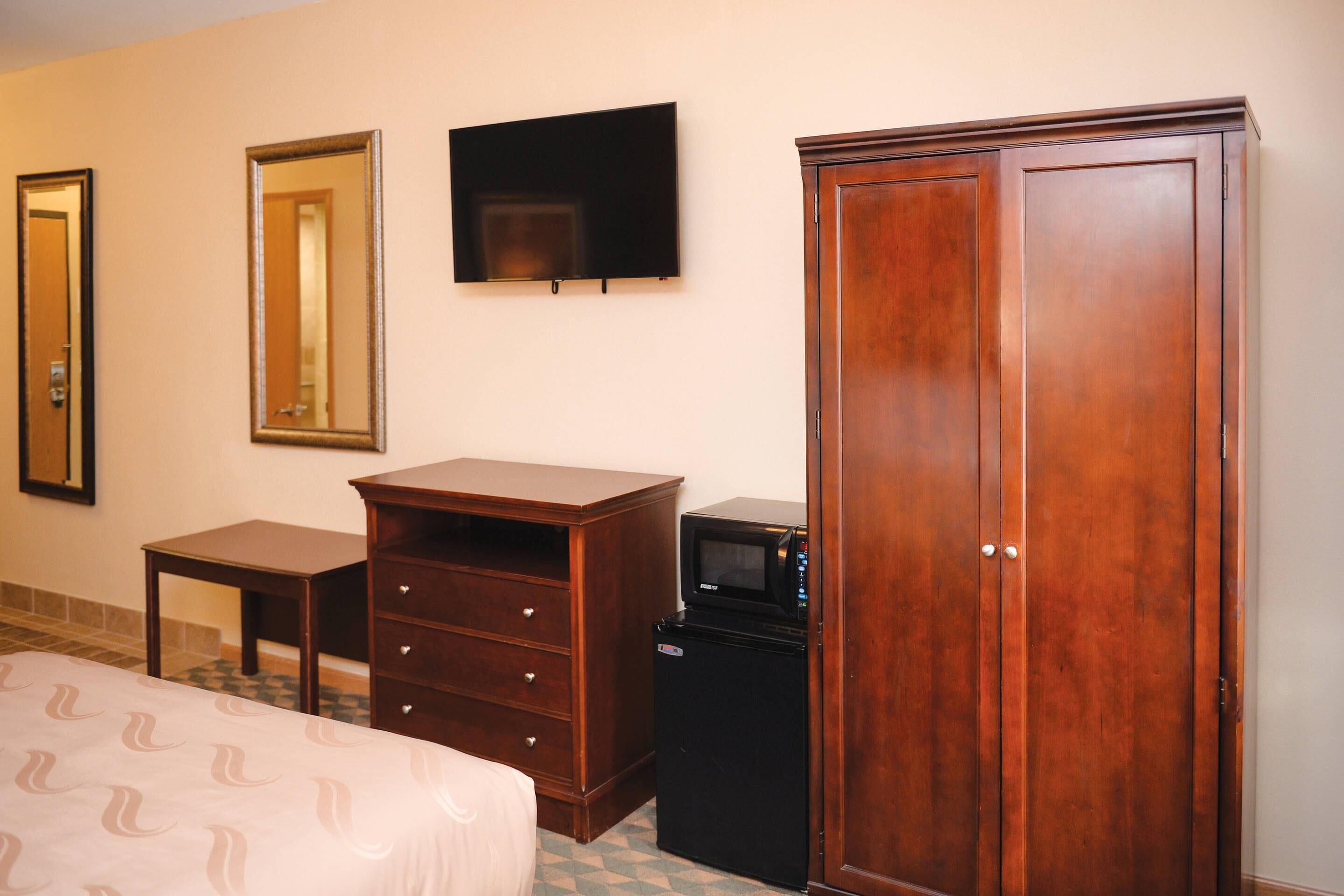 Una habitación de hotel con una cama, un aparador de madera, un televisor, un microondas y un armario.