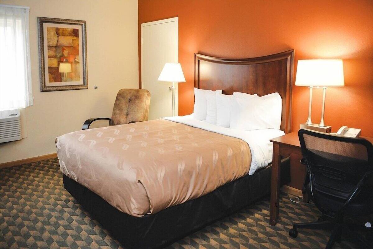 Una habitación de hotel con una cama, una silla, un escritorio y una lámpara.