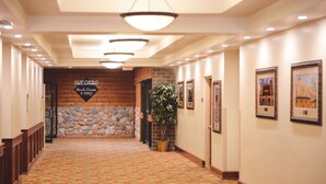 Un pasillo de hotel con alfombra estampada, paredes de madera, detalles de piedra y cuadros enmarcados.