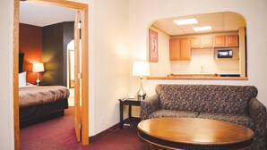 Una habitación de hotel con cama, sofá, una mesita, lámpara y una kitchenette equipada con armarios y microondas.