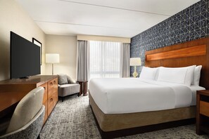 Una habitación de hotel con cama, escritorio, silla, televisor y ventana con cortinas.