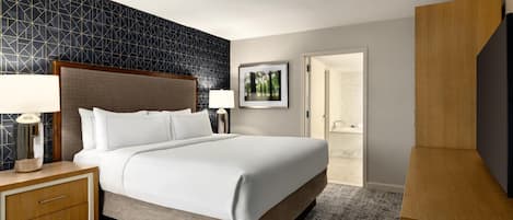 Habitación de hotel con una cama grande, dos mesitas de noche con lámparas, un cuadro enmarcado en la pared y un armario de madera.