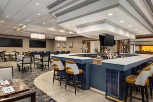 A hotel bar area with a counter, bar stools, and a television screen.