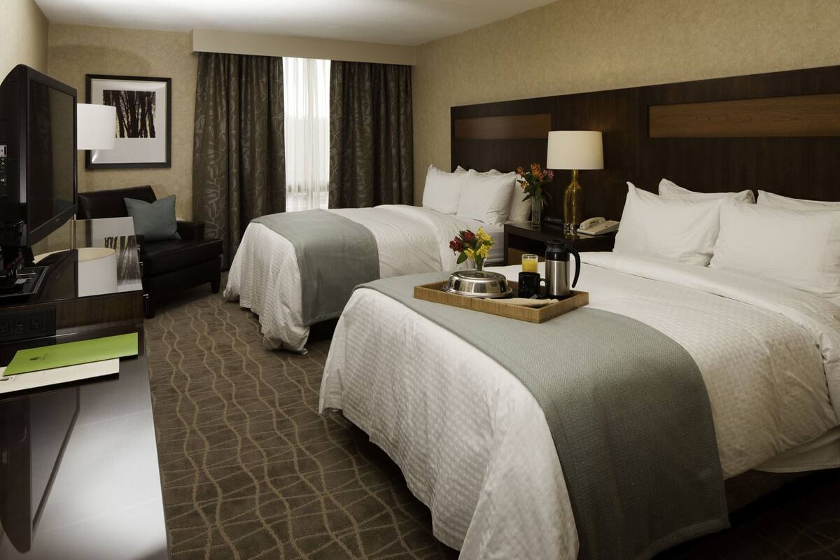 Ein Hotelzimmer mit zwei Betten, einem Schreibtisch mit Computer, einem Fernseher und einem Nachttisch mit Lampe und Telefon.