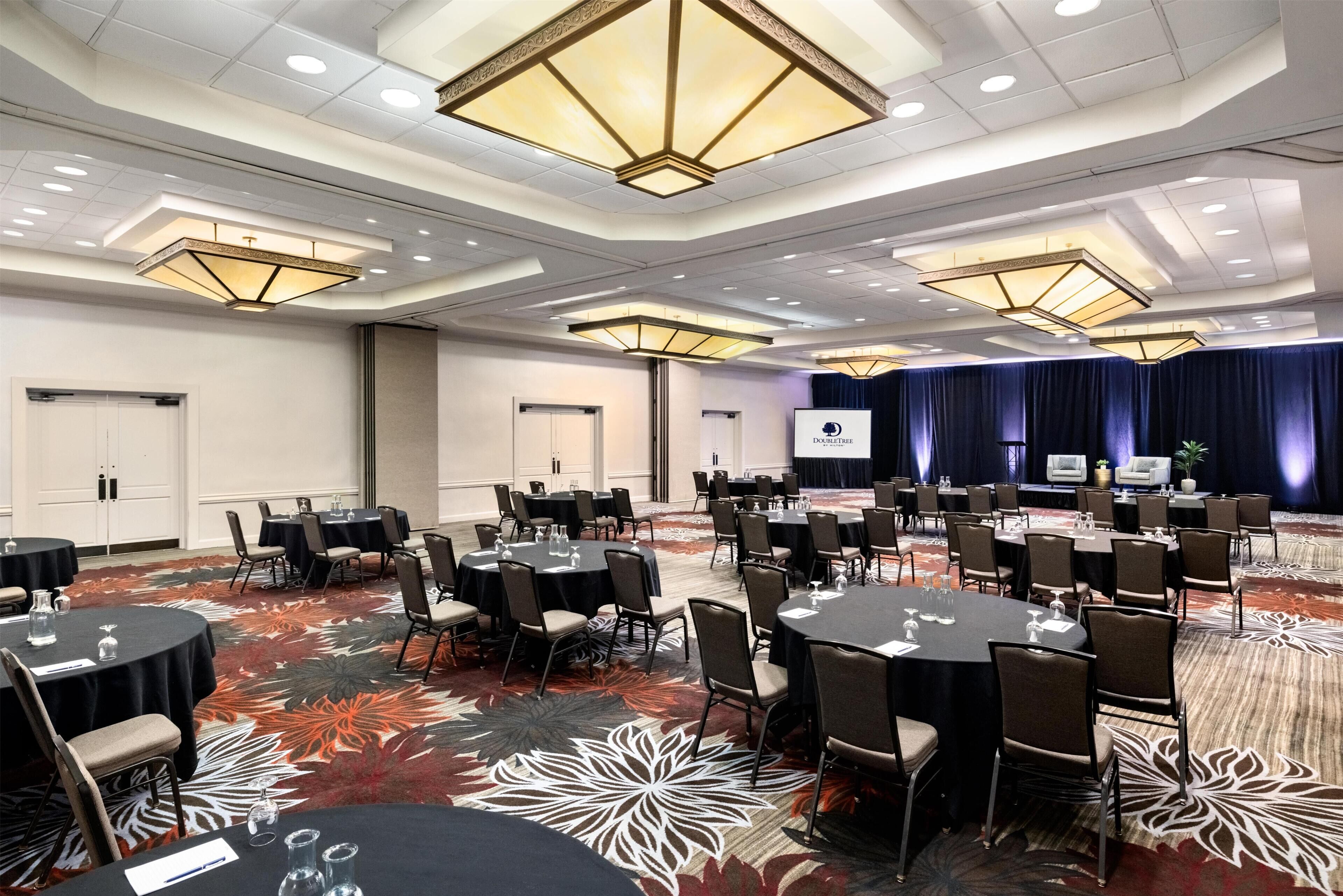 A conference room with round tables, chairs, and a stage with a screen.