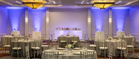 A banquet hall with round tables, chairs, and a bar area.