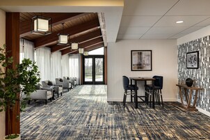 A hotel lobby with a patterned carpet, wooden ceiling beams, a reception desk, and seating area.