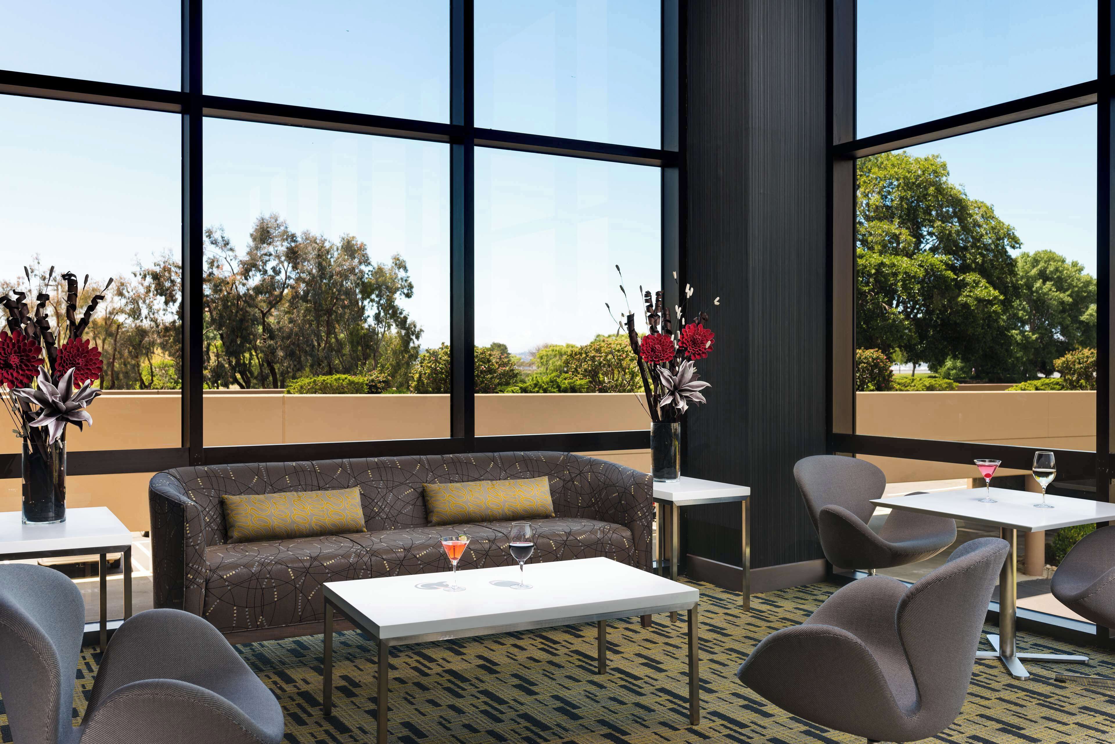 A modern outdoor seating area with a sofa, chairs, and a table, featuring a clear view of the surrounding landscape through large windows.