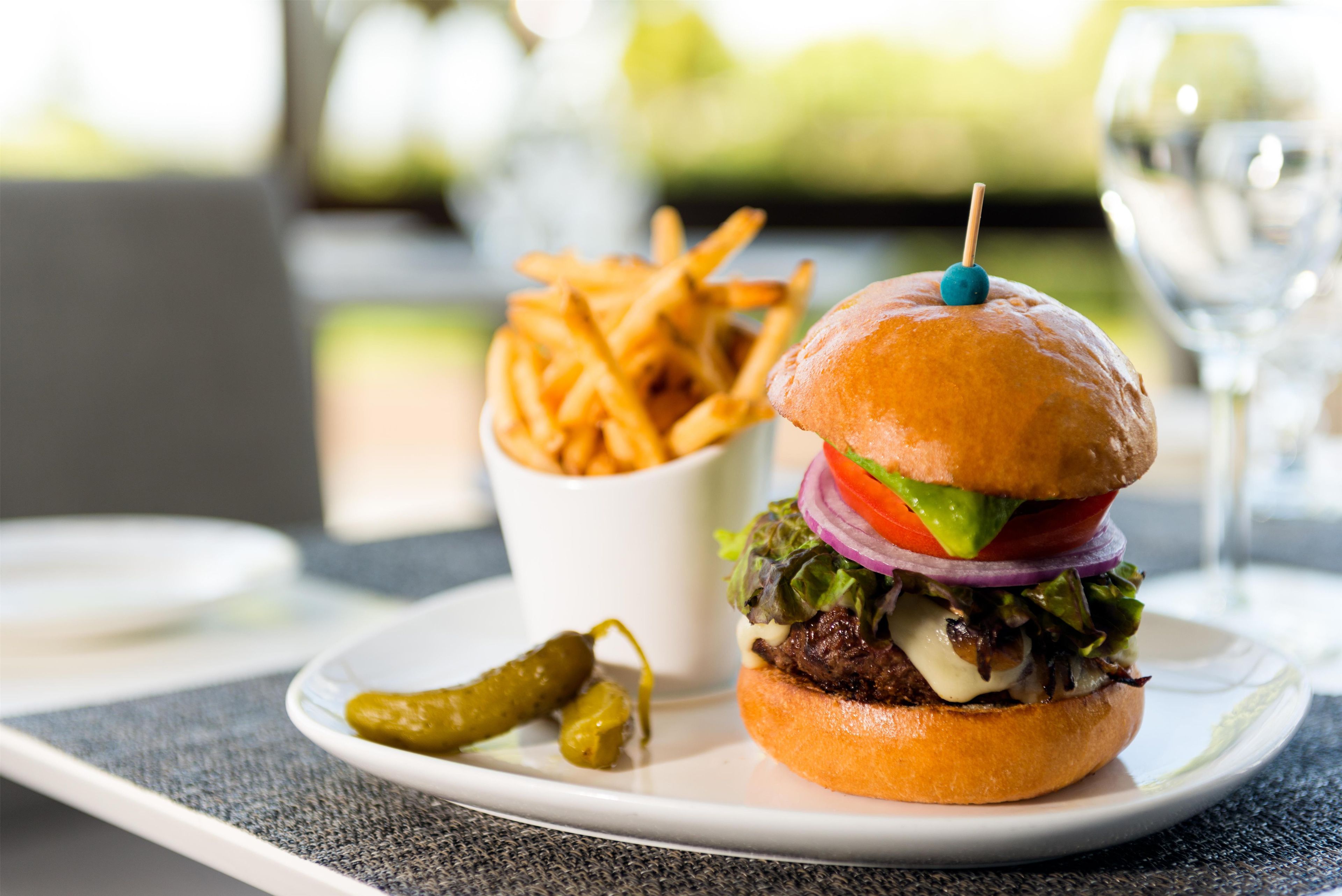 A meal consisting of a burger with a bun, lettuce, tomato, onion, and a beef patty, accompanied by a side of fries and pickles on a white plate.
