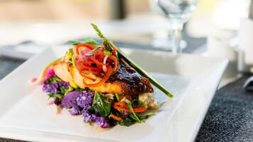 A plated dish with a variety of vegetables and a piece of meat, possibly salmon, on a rectangular white plate.
