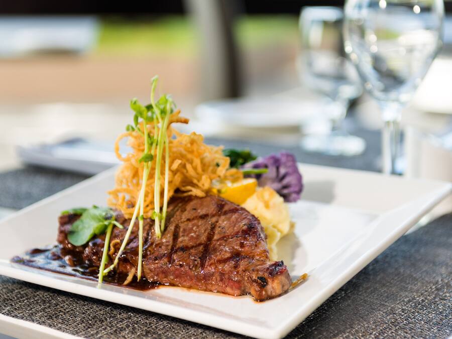 A steak with vegetables and sauce on a white plate.