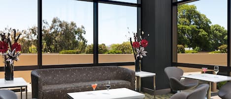 A modern lounge area with a sofa, chairs, and a table, featuring large windows and a view of greenery.