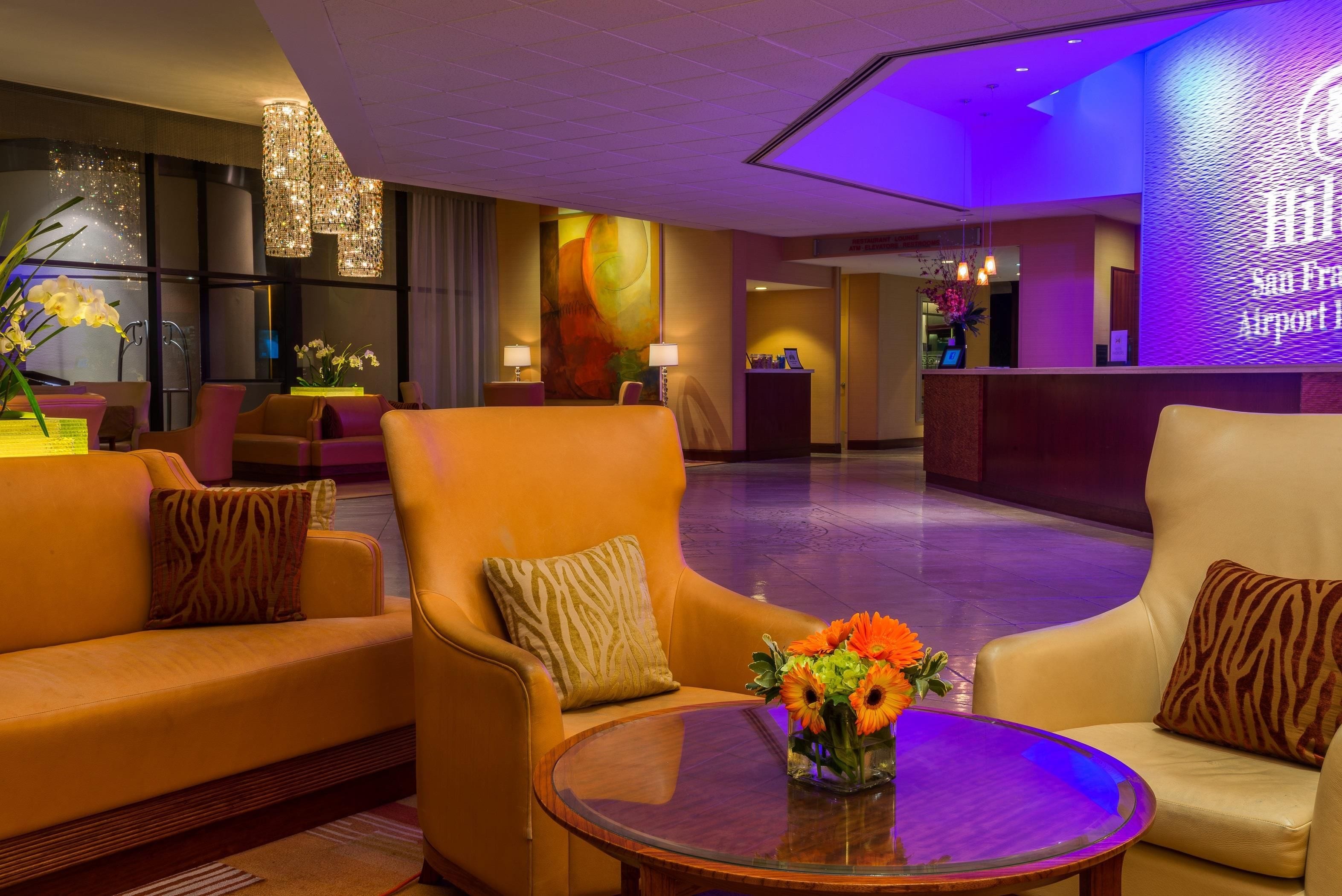Un hall de hotel con sofás de cuero, una mesa redonda con un jarrón de flores y un mostrador de recepción.
