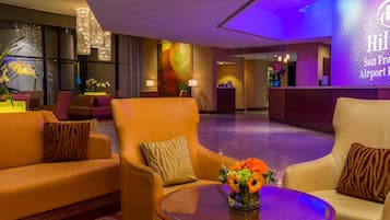 Un hall de hotel con sofás de cuero, una mesa redonda con un jarrón de flores y un mostrador de recepción.