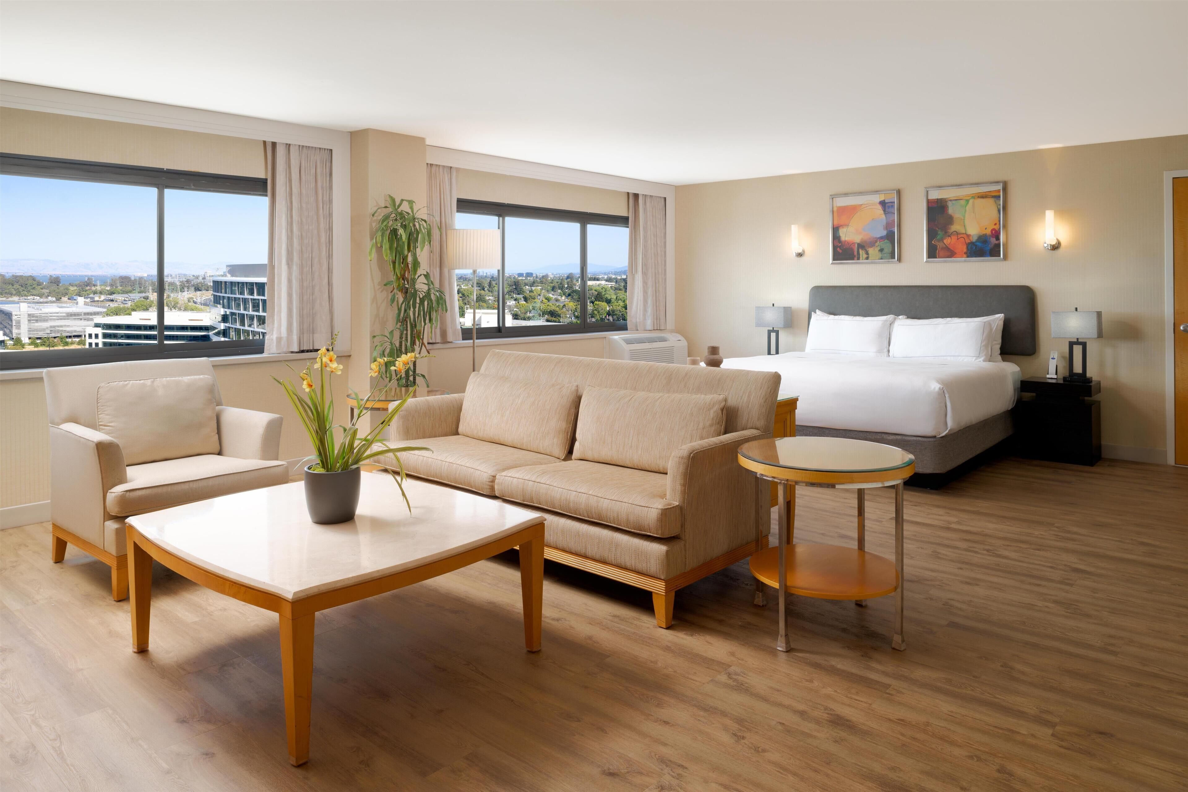 A hotel room with a bed, a sofa, a coffee table, and a view of the city.
