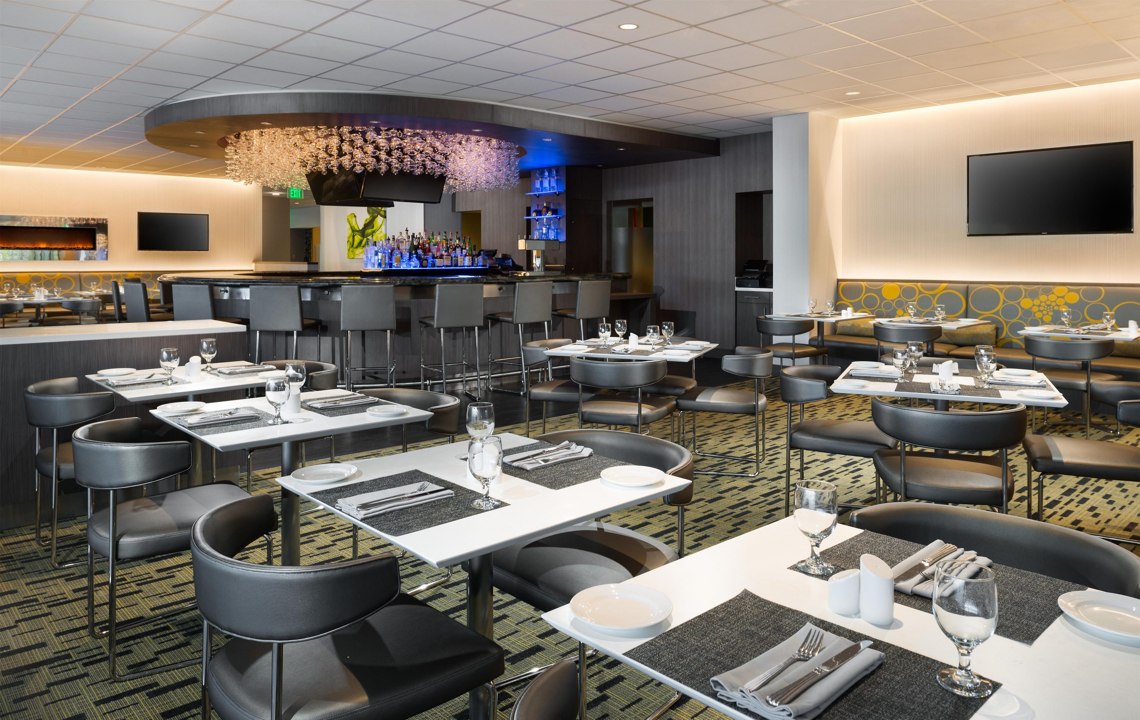 Ein Hotelrestaurant mit mehreren Tischen, einer Bar und einem großen Bildschirm.