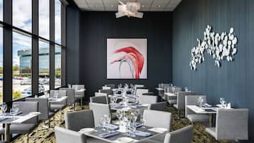 Un'elegante sala da pranzo con tavoli apparecchiati, ampie finestre e un'importante opera d'arte astratta alle pareti.