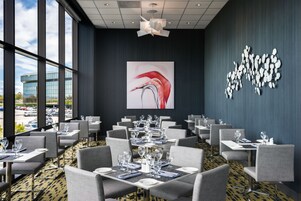 Un comedor moderno con mesas listas para el servicio, amplios ventanales y una destacada obra de arte abstracta en la pared.