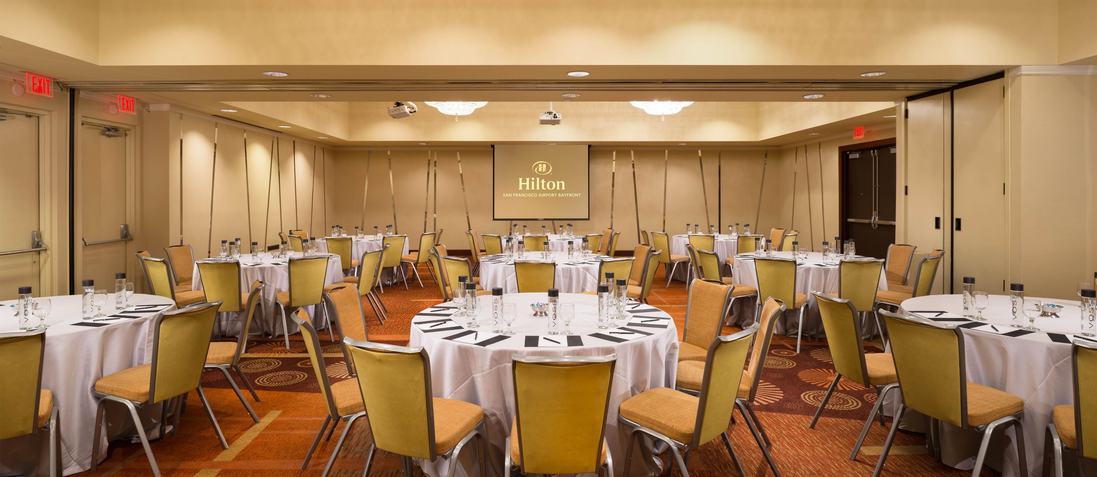 Un salón de conferencias con varias mesas y sillas, equipado con botellas de agua y vasos, en el Hilton San Francisco Airport Bayfront.