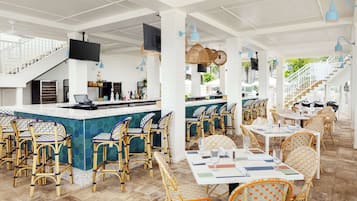 Un restaurante espacioso con techos altos, sillas de mimbre y una zona de bar central.