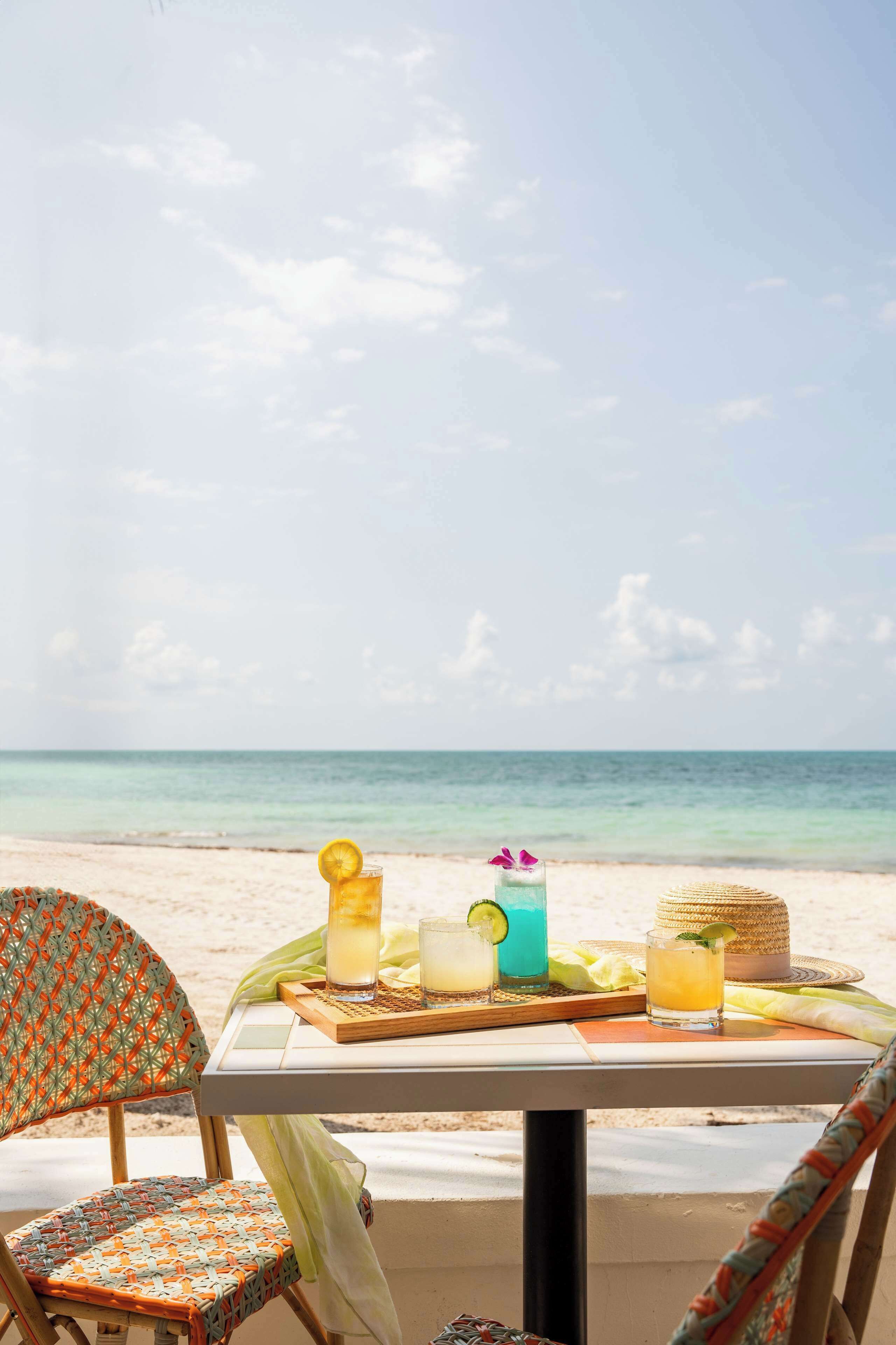 A beachside table with drinks and a straw hat, overlooking the ocean.