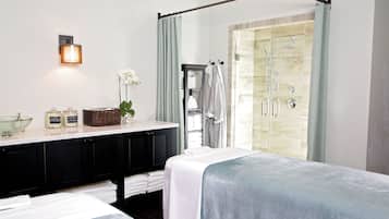 A modern bathroom with a glass shower enclosure, a vanity with a bowl sink, and two beds with white linens.