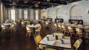 A spacious dining area with multiple tables and chairs, featuring a modern ceiling design and natural lighting from large windows.