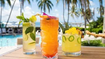 Three cocktails on a wooden table with a pool and palm trees in the background.