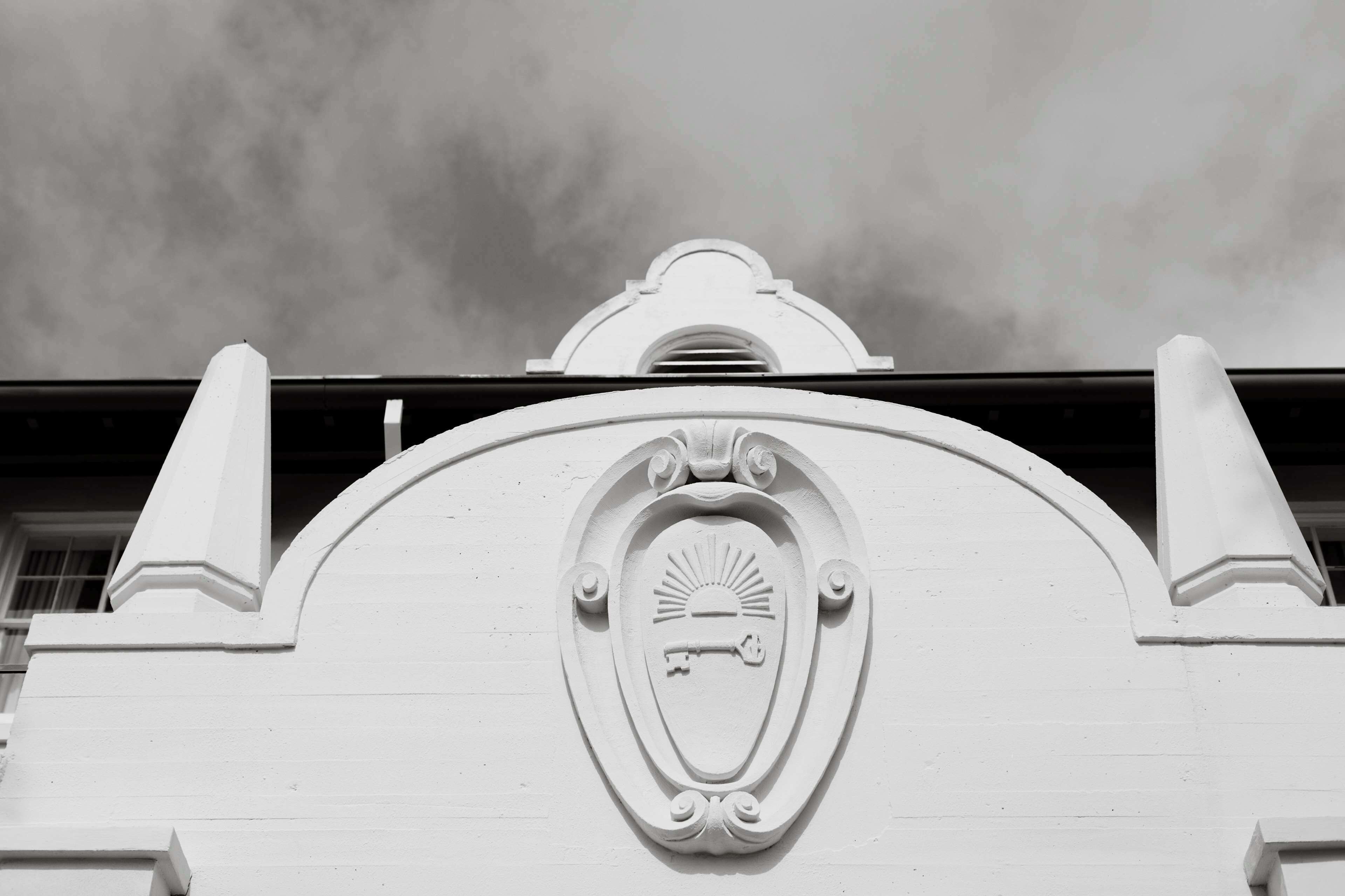 A white building with a decorative emblem featuring a sun and key.