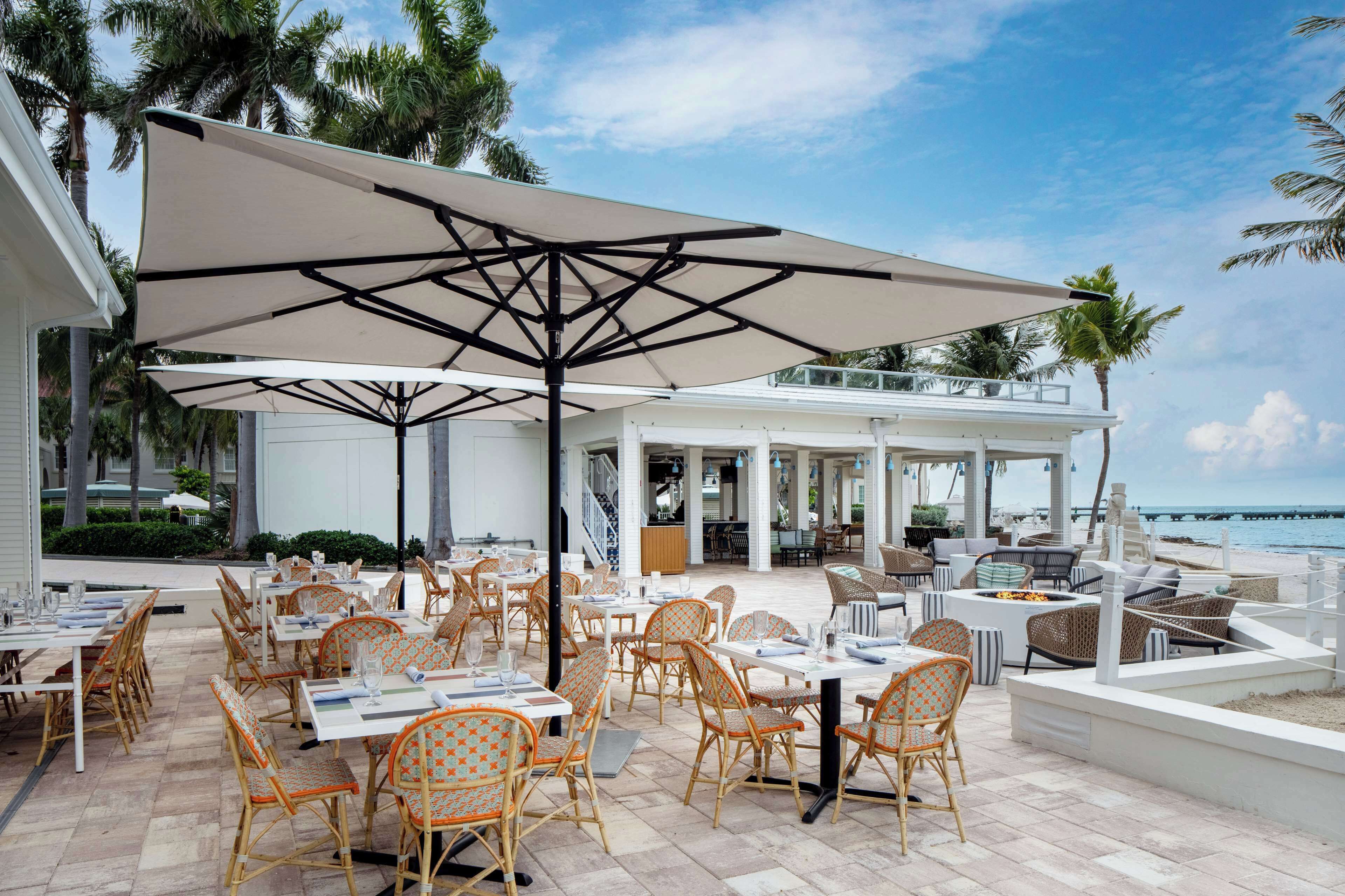 Un espace de restauration en plein air avec des chaises et des tables en osier, de grands parasols et une vue sur l’océan.