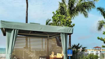 A sun loungers area with a covered seating area, palm trees, and a view of the ocean.