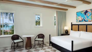Una habitación de hotel con una cama, dos sillas, una mesita, una mesita de noche con lámpara y un cuadro en la pared.