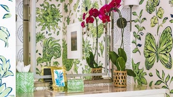 A vanity with a mirror, a small plant, a tissue box, and a framed picture on a white dresser.