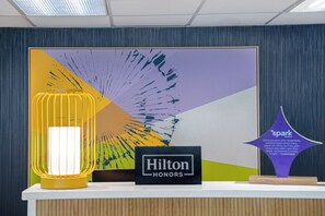 Un comptoir d’accueil agrémenté d’une œuvre d’art encadrée, d’une enseigne indiquant « Hilton HONORS » et d’une plaque commémorative du prix « Spark ».