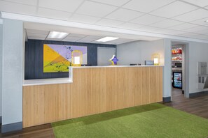 Un comptoir d’accueil avec un revêtement en bois, une moquette verte et un mur orné d’un tableau abstrait aux couleurs vives.