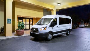Una camioneta blanca estacionada frente a un edificio con un letrero que indica 'No estacionar, descenso y abordaje de pasajeros'.
