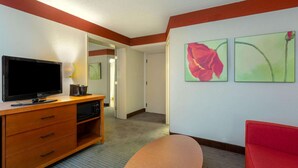 Habitación de hotel con televisor de pantalla plana, muebles de madera, una silla roja y dos cuadros con motivos florales en la pared.