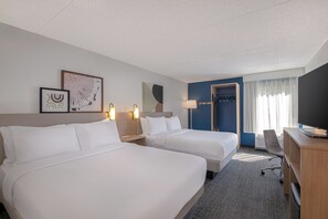 Habitación de hotel con dos camas, un escritorio, televisor y perchero.