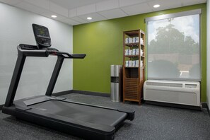 Une salle de sport équipée d’un tapis de course, d’une poubelle, d’une étagère avec des serviettes et d’une fenêtre donnant sur un beau paysage.