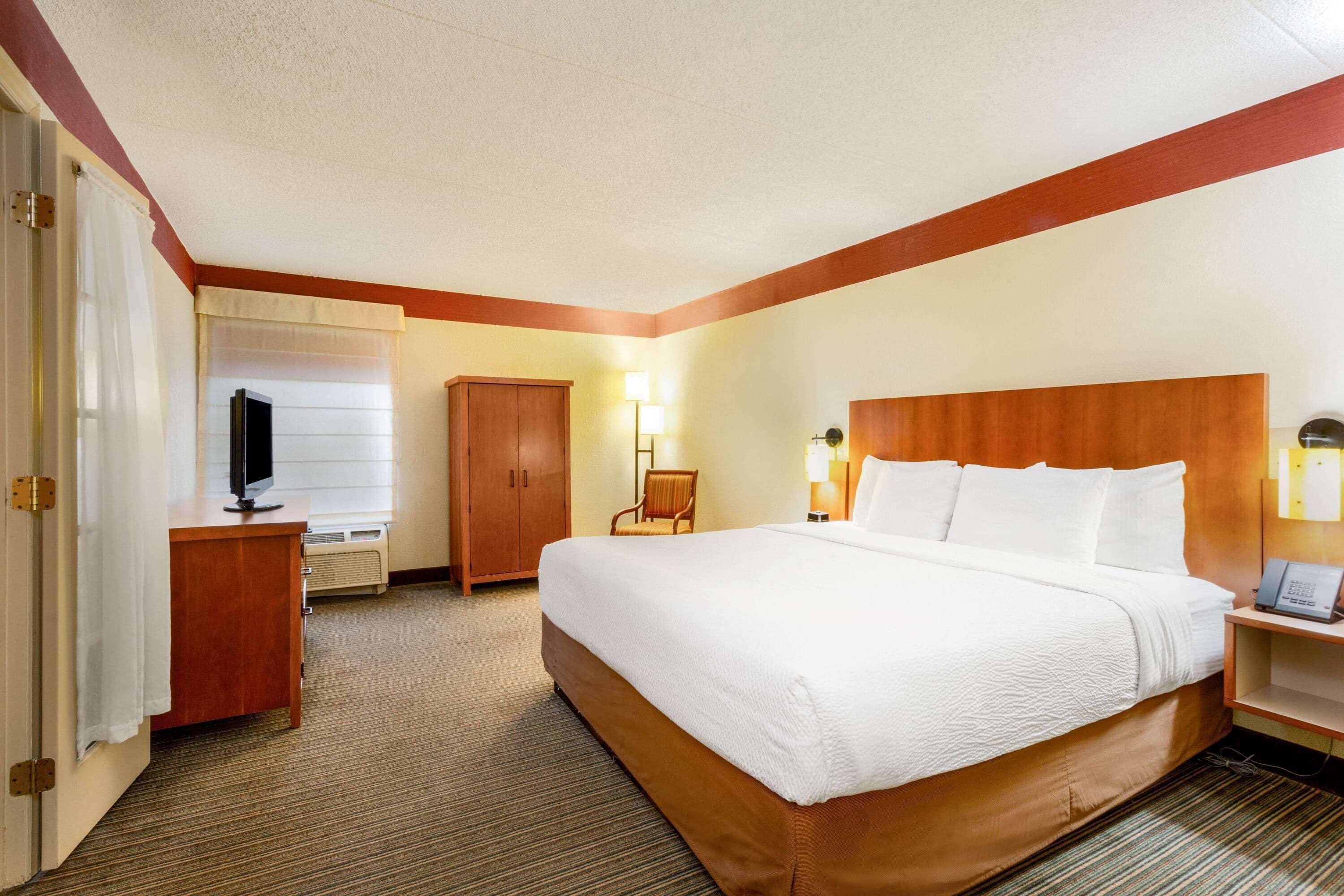 A hotel room with a bed, a desk, a chair, a television, and a lamp.