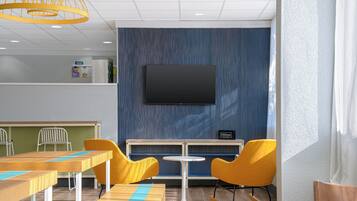 A hotel room with a flat-screen TV mounted on the wall, a small table with a chair, and a seating area with yellow chairs and a rocking chair.