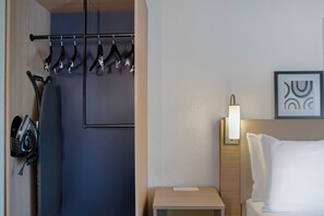 Une chambre d’hôtel comprenant un lit, une table de chevet, une lampe fixée au mur et un porte-manteau avec des cintres.