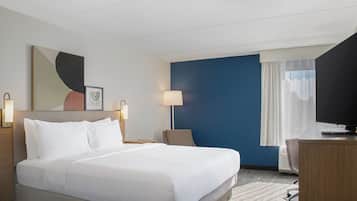 A hotel room with a bed, a desk, a chair, a television, and a window with curtains.