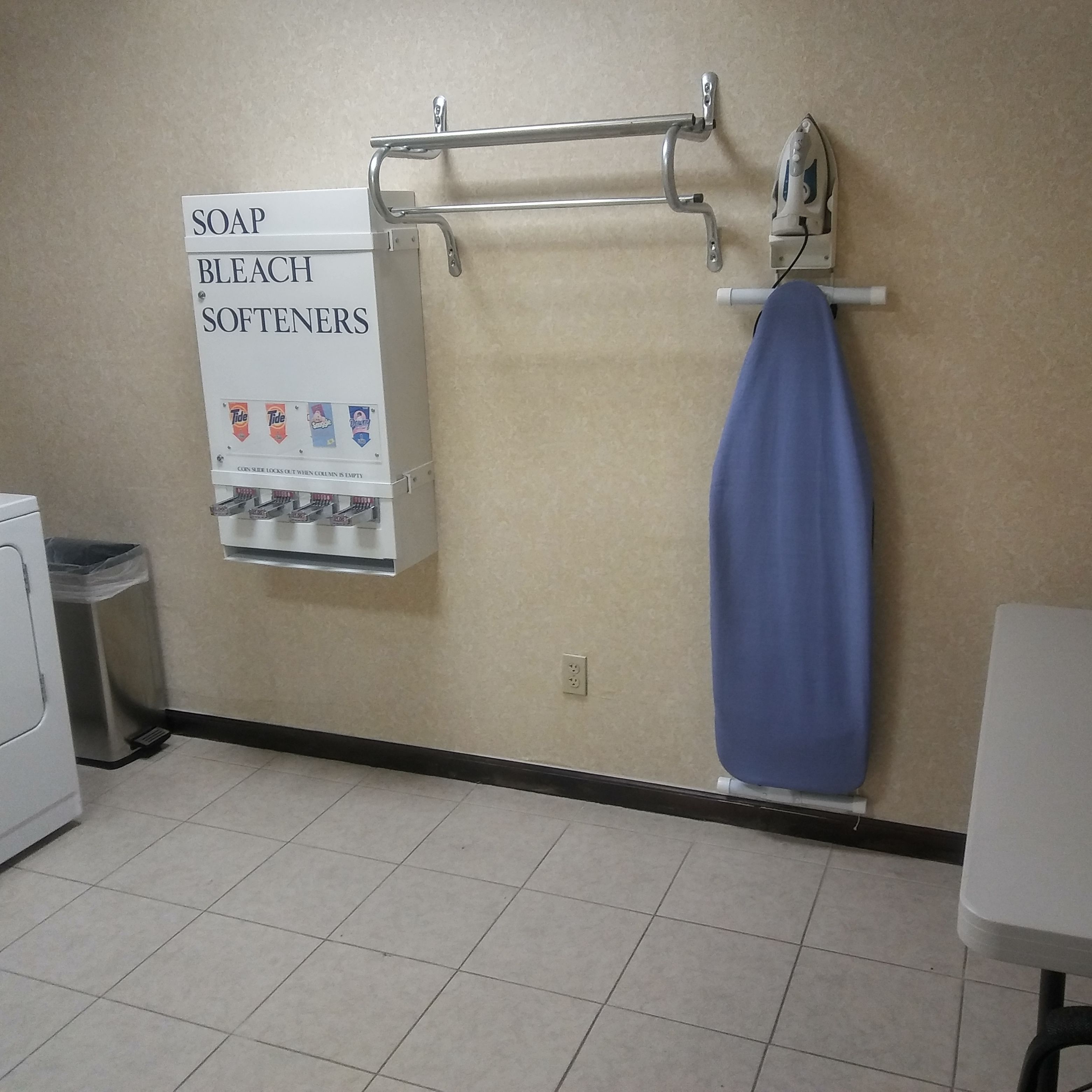 A bathroom with a soap and bleach softener dispenser, a blue towel hanging, and a washing machine.