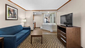 Habitación de hotel con sofá, televisión, una mesita, espejo y baño visible a través de una puerta abierta.